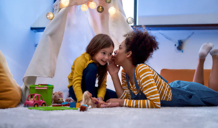 Woman whispering into a little girls ear, telling a secret.