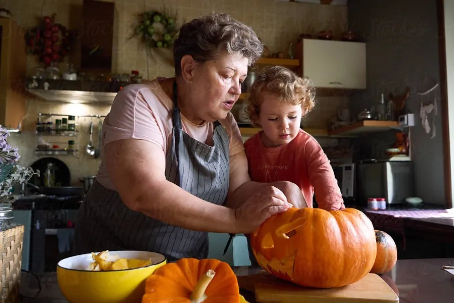 Grandmother and young child carving pumpkin in kitchen for Halloween