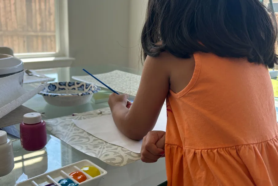 Child painting at glass table with watercolors