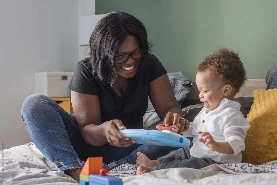 Smiling mother and toddler playing with a tablet in the bedroom