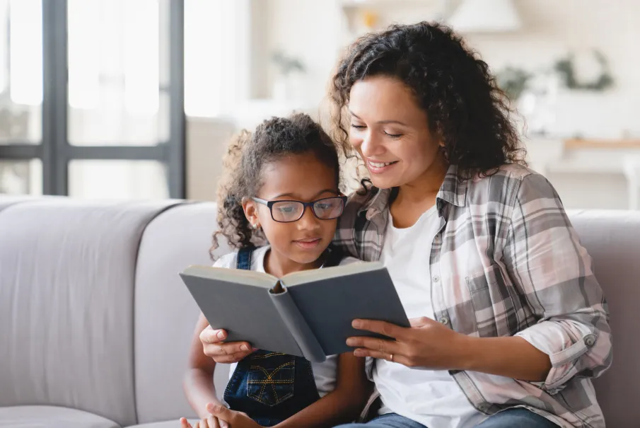 Mother reading book with daughter on couch