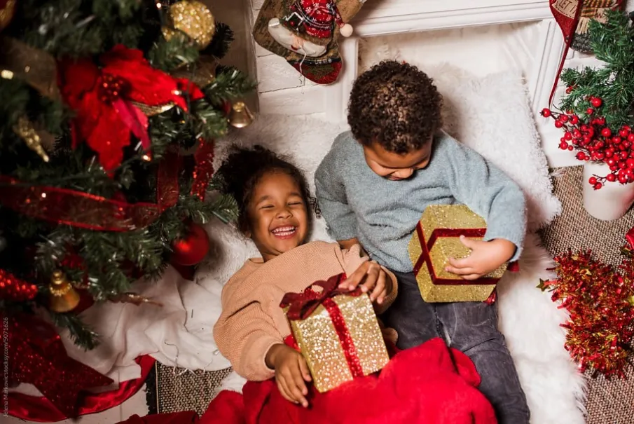 Two children exchanging Christmas gifts by a decorated tree